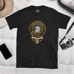 Puede incluir: Camiseta negra con un escudo de caballo blanco y el texto "Tait, Jefe de Tramile" en una pancarta dorada.