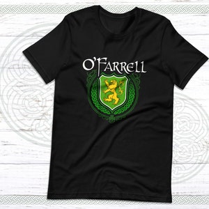 May include: Black t-shirt featuring the name "O'Farrell" in white script above a green and yellow crest. The crest displays a golden lion and intricate Celtic knotwork. The shirt is made of a soft material.