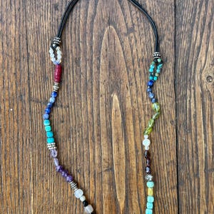 May include: A multi-colored beaded necklace with a leather cord and silver accents. The beads are arranged in a rainbow pattern, with shades of blue, green, yellow, orange, red, and purple.