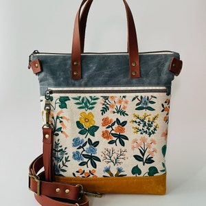May include: A blue and brown canvas tote bag with a floral print and a brown leather strap. The bag has a zipped pocket and a top handle.
