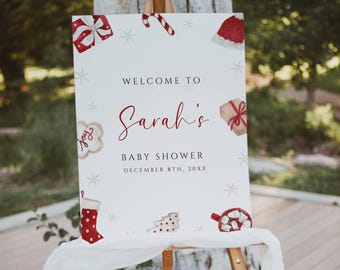May include: A wooden easel displays a white sign with Christmas-themed illustrations and the text "Welcome to Sarah's Baby Shower." The sign includes images of gifts, a stocking, and a Santa hat. The date is December 8th, 20XX.