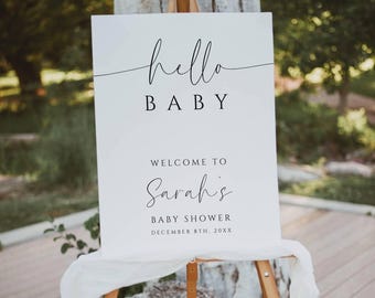 Pode incluir: Uma placa branca em um cavalete de madeira com as palavras "hello BABY" em escrita preta. Abaixo, lê-se "WELCOME TO Sarah's BABY SHOWER DECEMBER 8TH, 20XX". A placa é coberta com um pano branco, colocada ao ar livre em um deck de madeira.