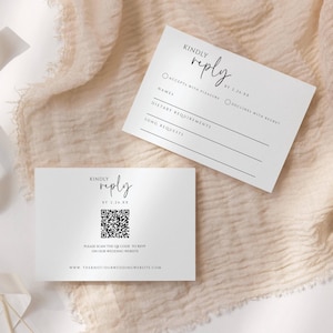 以下が含まれることがあります： 黒い文字で書かれた2枚の白いRSVPカード。上のカードには、招待状の承諾または辞退のためのチェックボックス、名前、食事の要望、歌のリクエストのためのスペースがあります。下のカードにはQRコードと「KINDLY REPLY BY 1.28.23 PLEASE SCAN THIS QR CODE TO RSVP OR CHOOSE WEDDING WEBSITE」というテキストがあります。