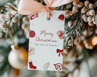 May include: A white gift tag with the words "Merry Christmas" and "The Smith Family" in red script, adorned with festive illustrations. The tag is tied with a light pink ribbon to a Christmas tree branch.