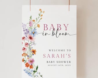May include: A rectangular sign with the text "BABY in bloom" and "WELCOME TO SARAH'S BABY SHOWER AUGUST 24TH, 20XX". The sign is decorated with a floral arrangement of pink, orange, blue, and purple flowers.