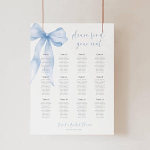 May include: A white seating chart with a watercolor blue bow and the text "please find your seat." The chart lists table numbers and names. The event is a bridal shower.