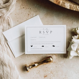 Puede incluir: Una tarjeta RSVP blanca con texto negro y un sobre a juego. La tarjeta incluye el texto "kindly RSVP" y solicita la elecci&oacute;n de comidas. Un sello de cera dorado se coloca debajo, sugiriendo un tema de boda o evento.