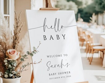 Pode incluir: Uma placa branca em um cavalete de madeira com as palavras "hello BABY" em letras pretas. Abaixo, lê-se "WELCOME TO Sarah's BABY SHOWER DECEMBER 8TH, 20XX". Um vaso de flores e capim-dos-pampas está à esquerda.