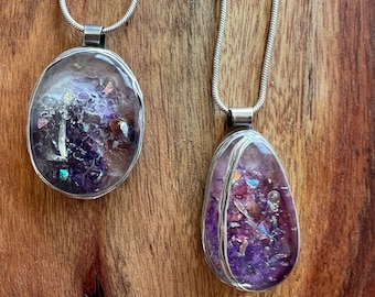 Può includere: Due collane con catena d'argento con ciondoli in resina viola e iridescente. I ciondoli sono di forma ovale e hanno un filo avvolto attorno al bordo.