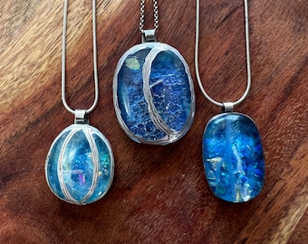 Può includere: Tre collane con catena d'argento con ciondoli ovali in vetro blu e iridescente incastonati in argento. I ciondoli hanno un aspetto testurizzato, di vetro craquelé.