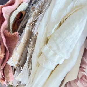 May include: A collection of fabric scraps in various textures and colors, including shades of cream, soft pink, tan, and brown. The pieces feature frayed edges, woven patterns, and solid surfaces, layered together to show a variety of textile materials.