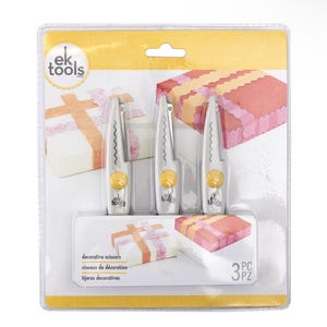 May include: A package of three decorative scissors. The scissors are silver with a yellow button and a wavy cutting edge. The package also shows examples of the scissors' use on decorative paper. The package has the text "ek tools" and "decorative scissors".