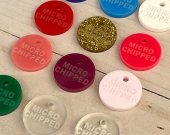 May include: A selection of brightly coloured, circular pet tags in shades of blue, red, pink, and green. Each tag features a small hole and the words "MICRO CHIPPED". One tag is gold glitter.
