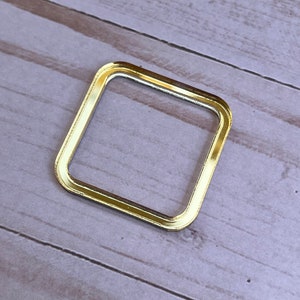 May include: A gold-colored square frame with a slightly raised edge. The frame is made of metal and has a smooth, polished finish.
