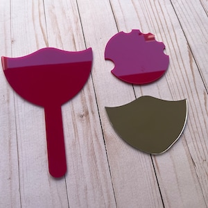 May include: Three pink acrylic mirrors, one shaped like a lollipop, one shaped like a circle with a bite taken out of it, and one shaped like a mustache.