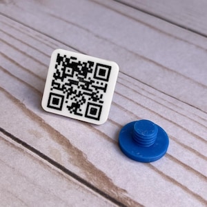 May include: A white square with a black QR code on it. A blue plastic screw with a round head is next to the square.