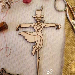 May include: A wooden cutout of a whimsical character wearing a top hat and a tuxedo, holding a pipe. The character is standing on a stick and has a whimsical, almost cartoonish appearance. The cutout is on a light brown background with the letter "B2" written in black below it.