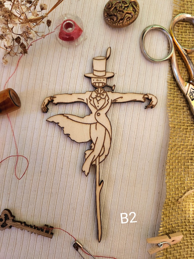 May include: A wooden cutout of a whimsical character wearing a top hat and a tuxedo, holding a pipe. The character is standing on a stick and has a whimsical, almost cartoonish appearance. The cutout is on a light brown background with the letter "B2" written in black below it.
