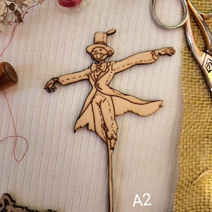 May include: Wooden cutout of a scarecrow wearing a top hat and a suit, with arms outstretched. The cutout is on a light brown background with the text "A2" in the bottom right corner.