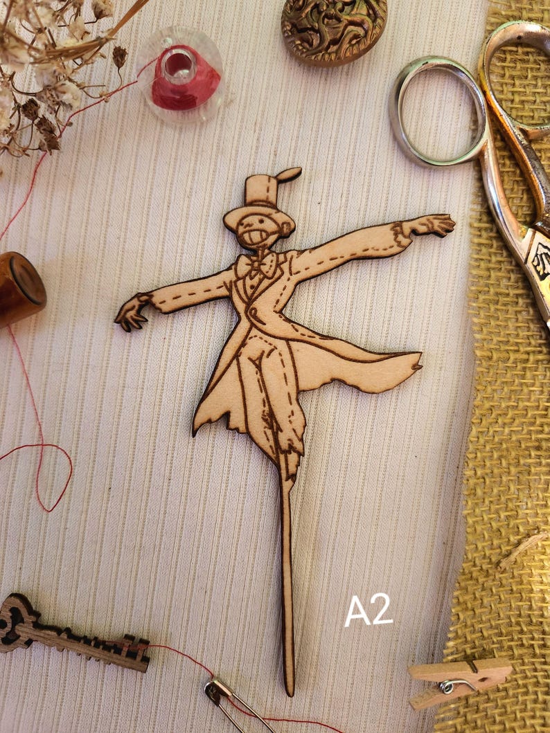 May include: Wooden cutout of a scarecrow wearing a top hat and a suit, with arms outstretched. The cutout is on a light brown background with the text "A2" in the bottom right corner.