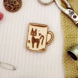 May include: A wooden mug with a black cat design. The mug is on a white fabric background.