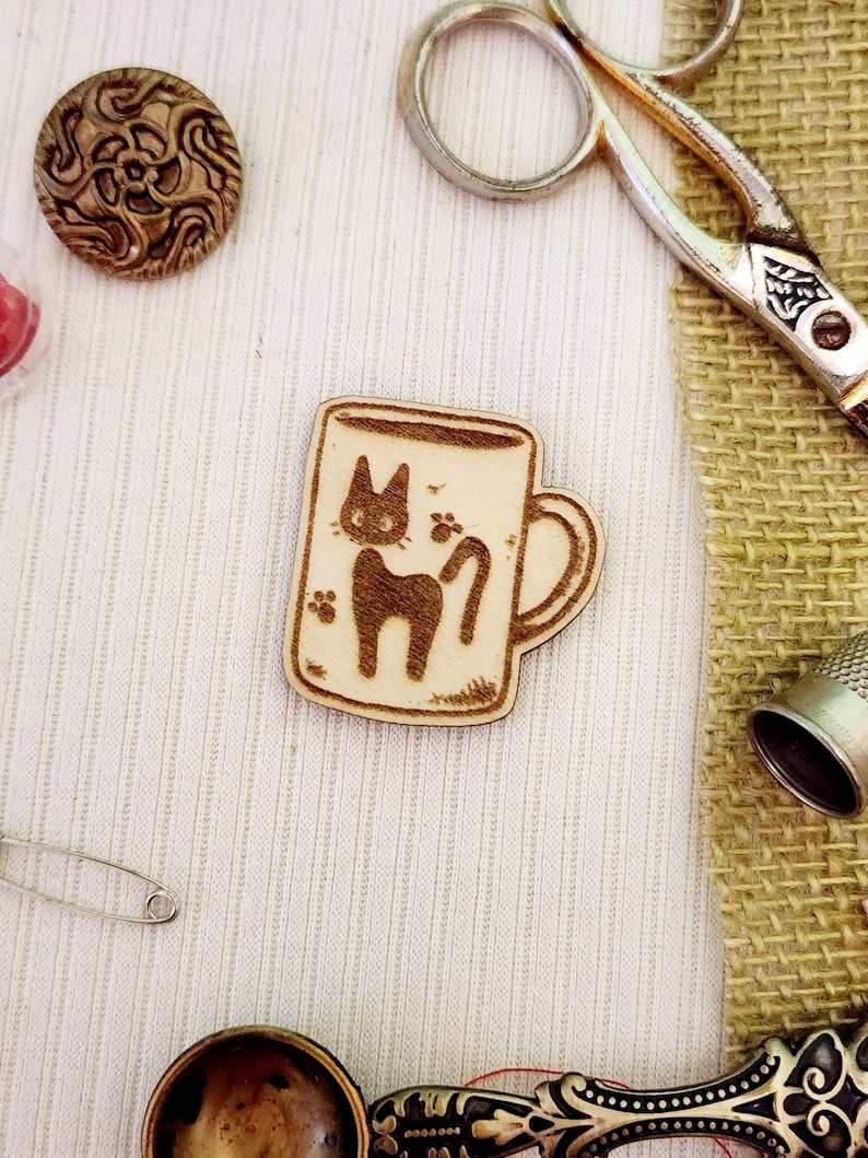May include: A wooden mug with a black cat design. The mug is on a white fabric background.