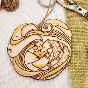 May include: A wooden heart-shaped ornament with a laser-cut design of a woman and a wolf cuddling. The design is in shades of brown and yellow.