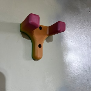 May include: A 3D printed wall mount with two hooks, painted in a gradient of pink, orange, and green.