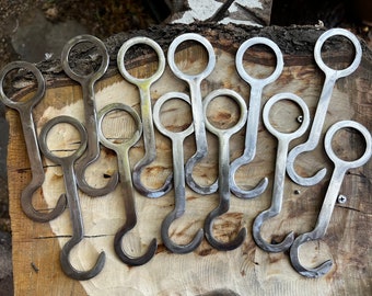 May include: A group of ten metal bottle openers with a circular handle and a hook at the end. The openers are arranged on a wooden surface.