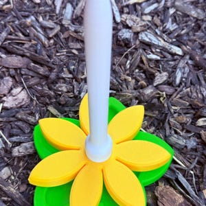 May include: A decorative bottle stopper in the shape of a flower. It has a white stem and a flower with yellow petals and green leaves. The stopper is made of plastic and is designed to fit into a bottle.