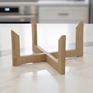 May include: A light-colored wooden plant stand with a cross-shaped base and four upright supports. The stand is made of natural wood and has a simple, modern design. The stand is designed to hold a plant pot.