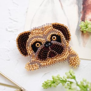 Può includere: Spilla artigianale a forma di carlino, realizzata con piccole perline colorate. La spilla presenta un volto di carlino dettagliato con orecchie, occhi e naso marroni scuri, e un corpo marrone e beige.