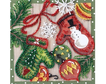 May include: A close-up of a beaded Christmas ornament with a snowman design. The ornament is red and white with a green beaded pine tree on the side. The ornament is surrounded by other beaded ornaments, including a green and red mitten and a red and yellow ornament.