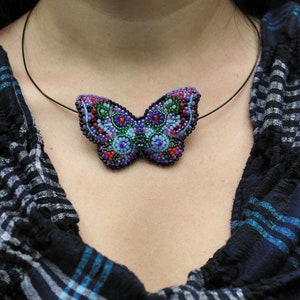 May include: A beaded butterfly pendant necklace with a black cord. The butterfly is made of purple, blue, green, and red beads.