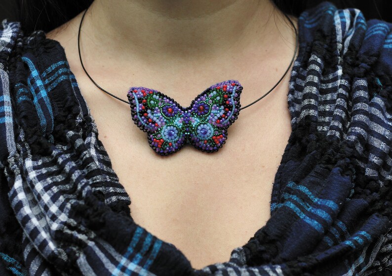 May include: A beaded butterfly pendant necklace with a black cord. The butterfly is made of purple, blue, green, and red beads.