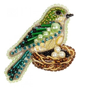 Könnte beinhalten: Eine Brosche in Form eines Vogels aus grünen und goldenen Perlen mit einem Nest aus Perlen. Der Vogel sitzt auf einem Nest aus braunen und goldenen Perlen.