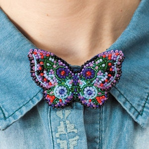 May include: A beaded butterfly brooch with a colorful design featuring shades of purple, green, blue, red, and black.
