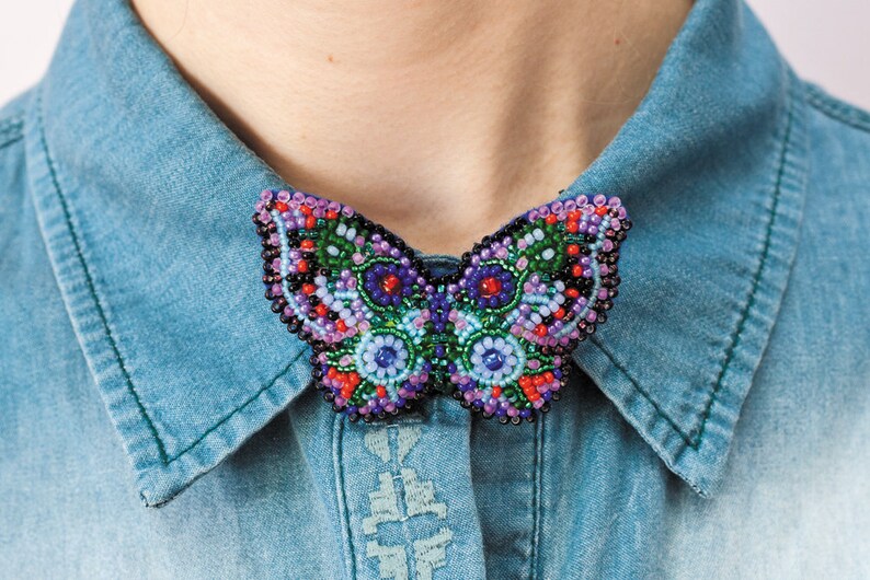 May include: A beaded butterfly brooch with a colorful design featuring shades of purple, green, blue, red, and black.