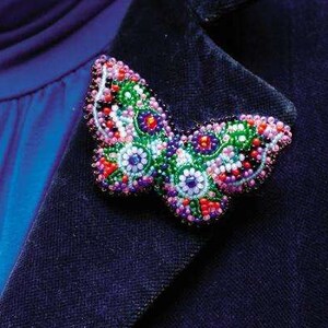 May include: A beaded butterfly brooch with pink, green, blue, and red beads. The brooch is attached to a dark blue fabric.