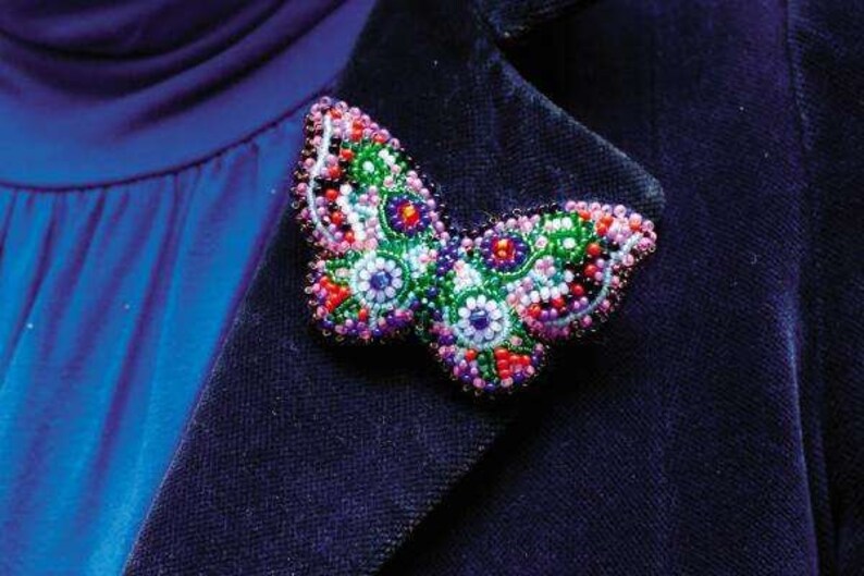 May include: A beaded butterfly brooch with pink, green, blue, and red beads. The brooch is attached to a dark blue fabric.