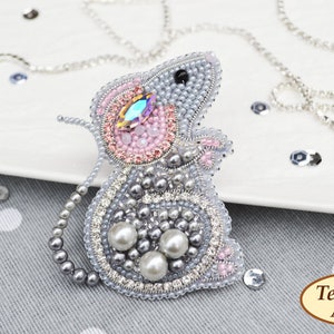 May include: A grey beaded mouse brooch with pink and silver accents. The mouse has a large crystal eye and is decorated with pearls.