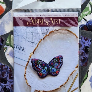 May include: A bead embroidery kit featuring a butterfly design. The butterfly is made of colorful beads and is approximately 70mm x 40mm. The kit includes 656 beads and is labeled "AD-001".