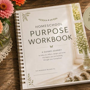 May include: A spiral-bound Homeschool Purpose Workbook with a white cover featuring black text, floral accents, and a window scene. The cover includes the title, a subtitle, and a line for a name. A black pen rests beside the workbook on a wooden surface.
