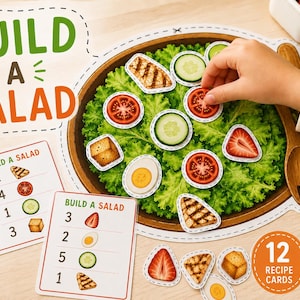 Puede incluir: Un set educativo Build a Salad que incluye un plato de papel grande con lechuga verde, cubiertos de madera para ensalada y varios ingredientes de papel como tomate, pepino, huevo y pollo a la parrilla, junto a tarjetas de recetas.