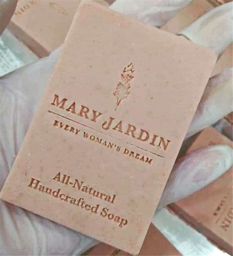 Puede incluir: Una barra de jab&oacute;n rosa con el texto "MARY JARDIN EVERY WOMAN'S DREAM All-Natural Handcrafted Soap" impreso en ella.