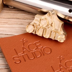 以下が含まれることがあります： 「EDAL OUTS」という文字が浮き彫りになった真鍮製のスタンプ。このスタンプは、カスタムロゴ入りの革製品を作るために使用されます。