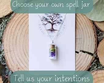 Puede incluir: Un collar plateado con un pequeño colgante de tarro de cristal lleno de elementos morados y verdes. El tarro está suspendido de una cadena, con texto que dice "Choose your own spell jar" y "Tell us your intentions".