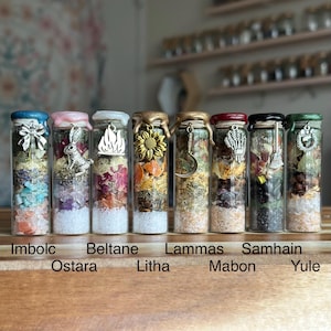 Puede incluir: Siete botellas de vidrio llenas de capas de hierbas coloridas, cristales y sales. Cada botella tiene un dije decorativo y una tapa. Las botellas están etiquetadas con las palabras "Imbolc", "Ostara", "Beltane", "Litha", "Lammas", "Mabon" y "Yule".