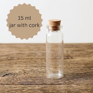 Op de afbeelding: Een heldere glazen pot met een kurk. De pot is cilindrisch en heeft een inhoud van 15 ml. De tekst "15 ml jar with cork" staat in een bruinachtige cirkel.
