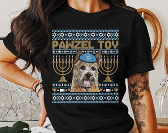 May include: Black t-shirt featuring a dog wearing a blue yarmulke, with the text "PAWZEL TOY" above a menorah design. The design has a blue and white pattern, creating a festive holiday theme.